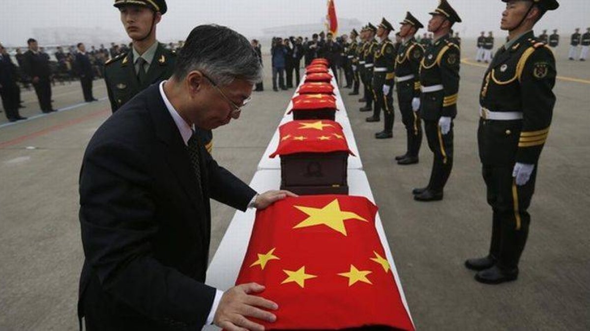 El embajador chino en Seul cubre los ataudes con la bandera de China, durante la ceremonia.