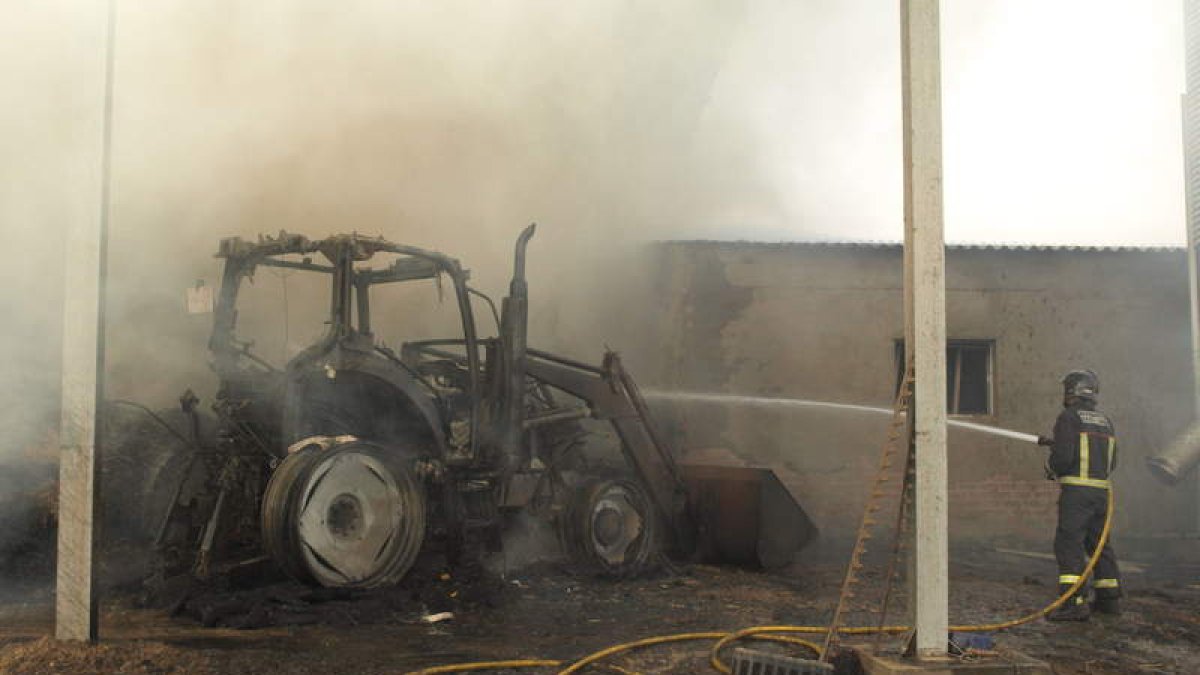 Un bombero culmina la extinción de las llamas que carbonizaron el tractor.