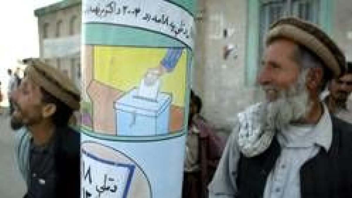 Dos hombres afganos pasan por delante de uno de los carteles electorales en Kabul