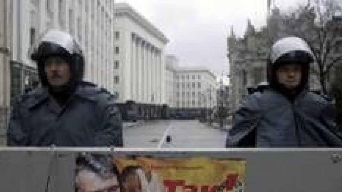 Dos policíaas vigilan una calle vacía de Kiev parapetados tras una valla con un póster de Yúschenko