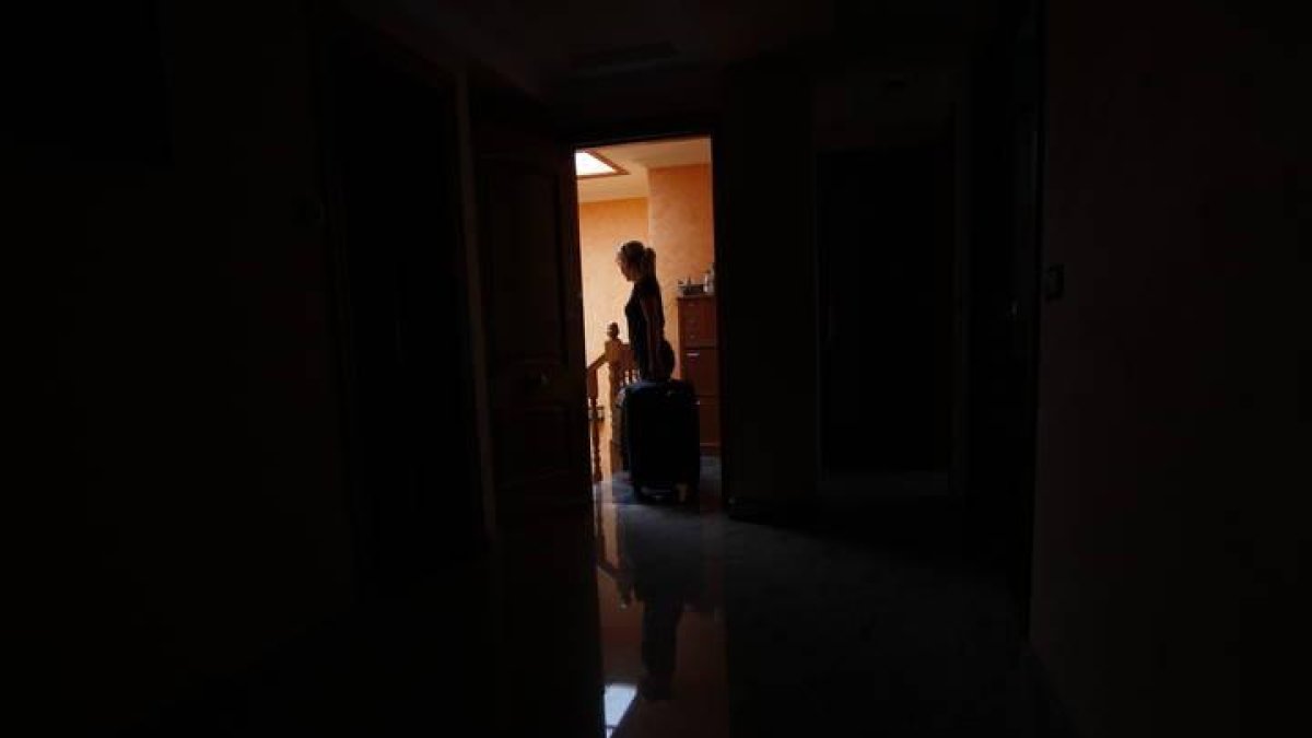 Una mujer sale de su vivienda con una maleta.
