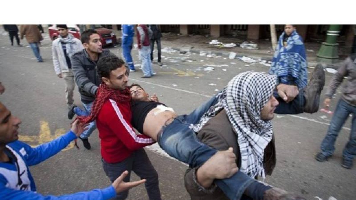 Unos manifestantes ayudan a un joven herido en los disturbios con la policía cerca de la plaza Tahrir, en El Cairo, hoy.