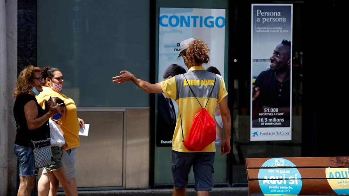 Un agente cívico conmina al uso de la mascarilla en una calle de Hospitalet. TONI ALBIR
