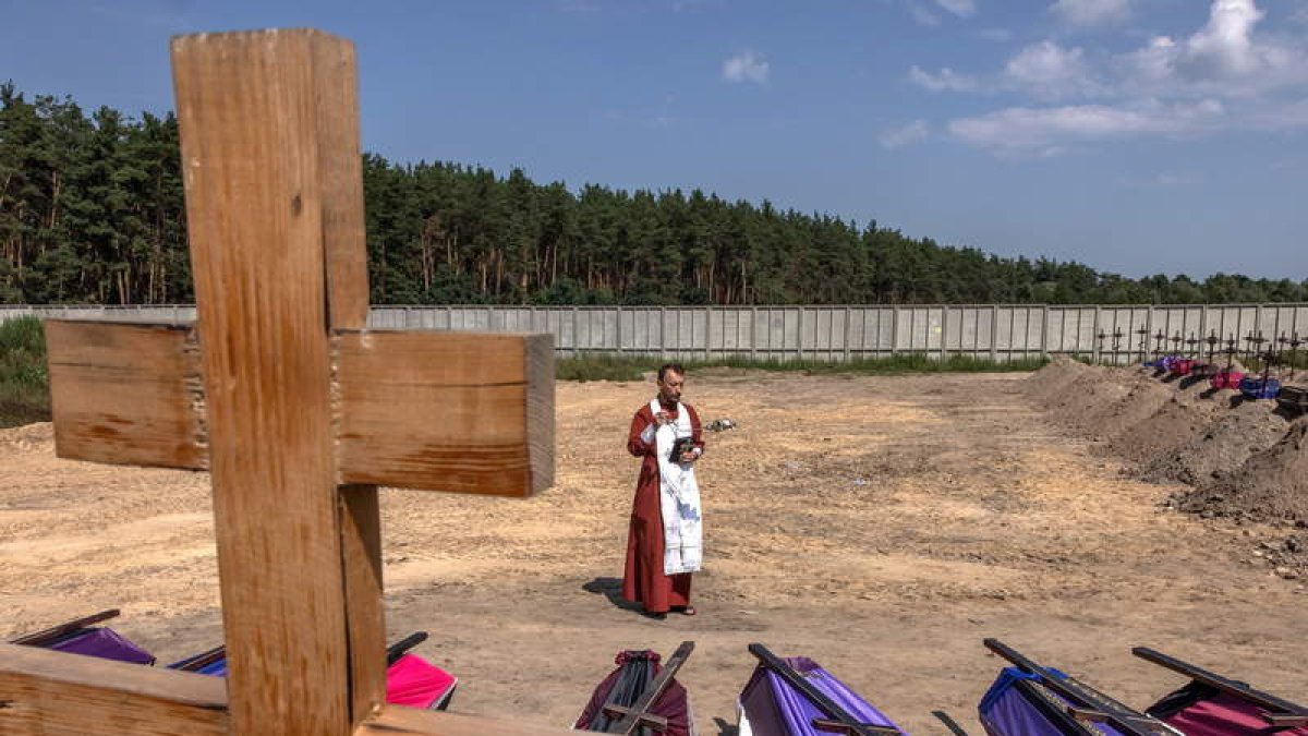 Un cura ortodoxo bendice féretros en la fosas abiertas en el cementerio de Bucha. ROMAN PILIPEY