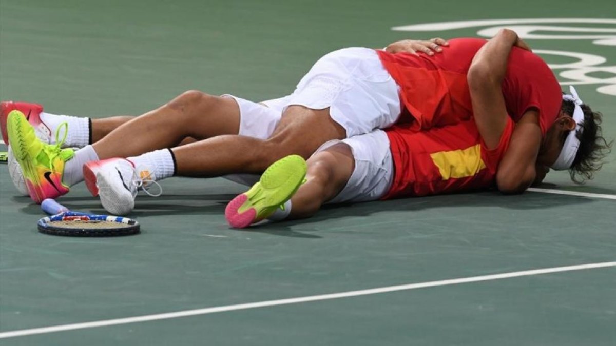 Rafa Nadal y Marc López se abrazan en el suelo tras clasificarse para la final olímpica.