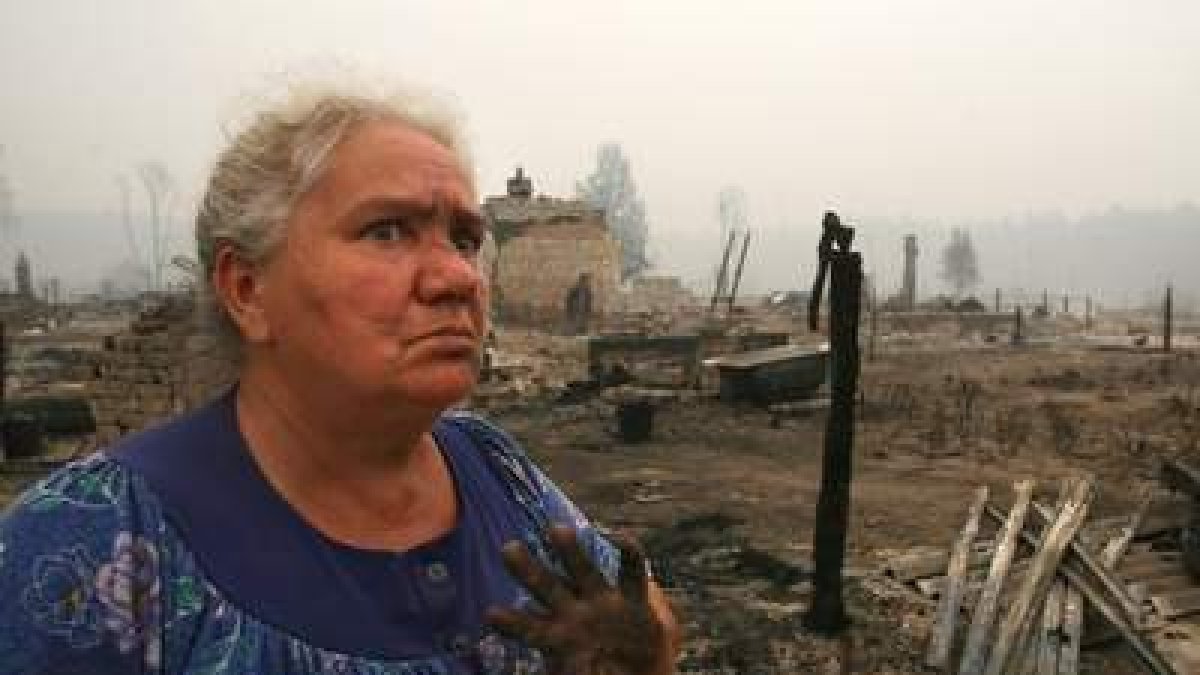 Una mujer posa delante de los restos de su pueblo, asolado por los incendios.