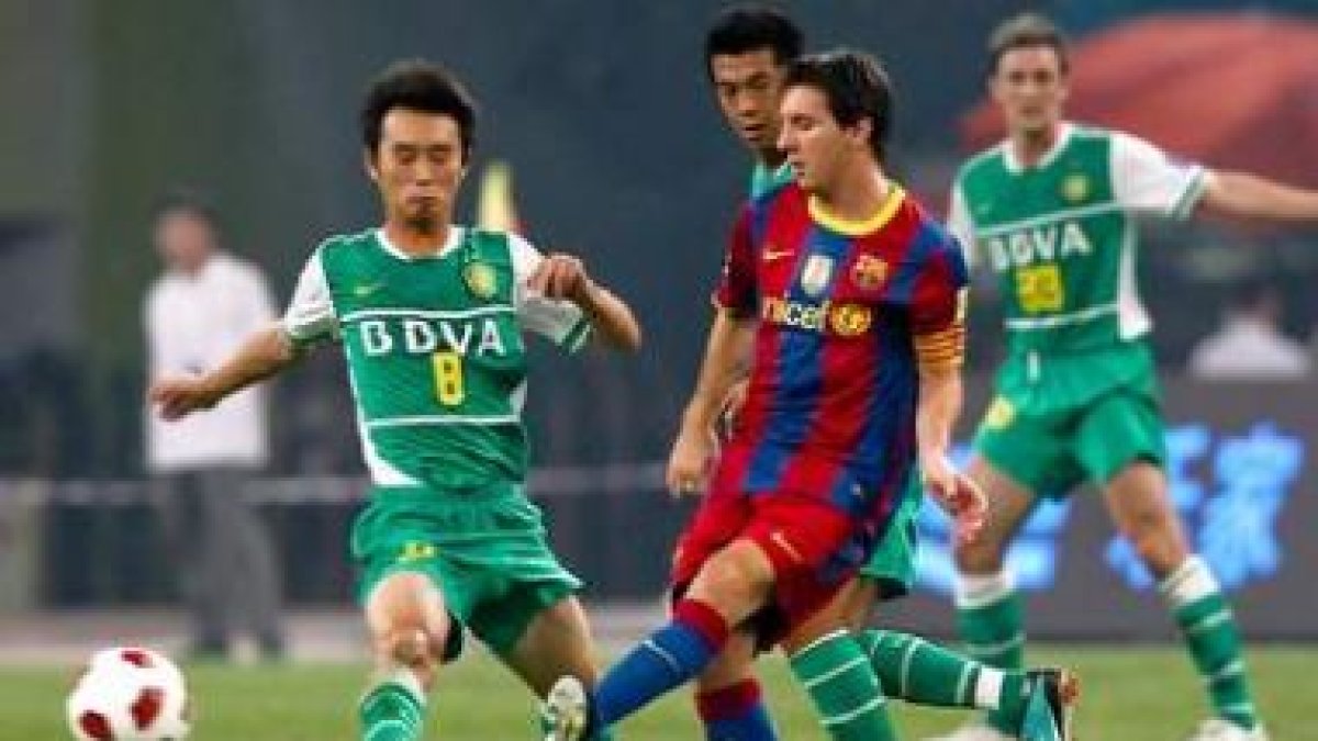 Lionel Messi (derecha), controla el balón ante el jugador del Beijing Guo, Yang Hao.