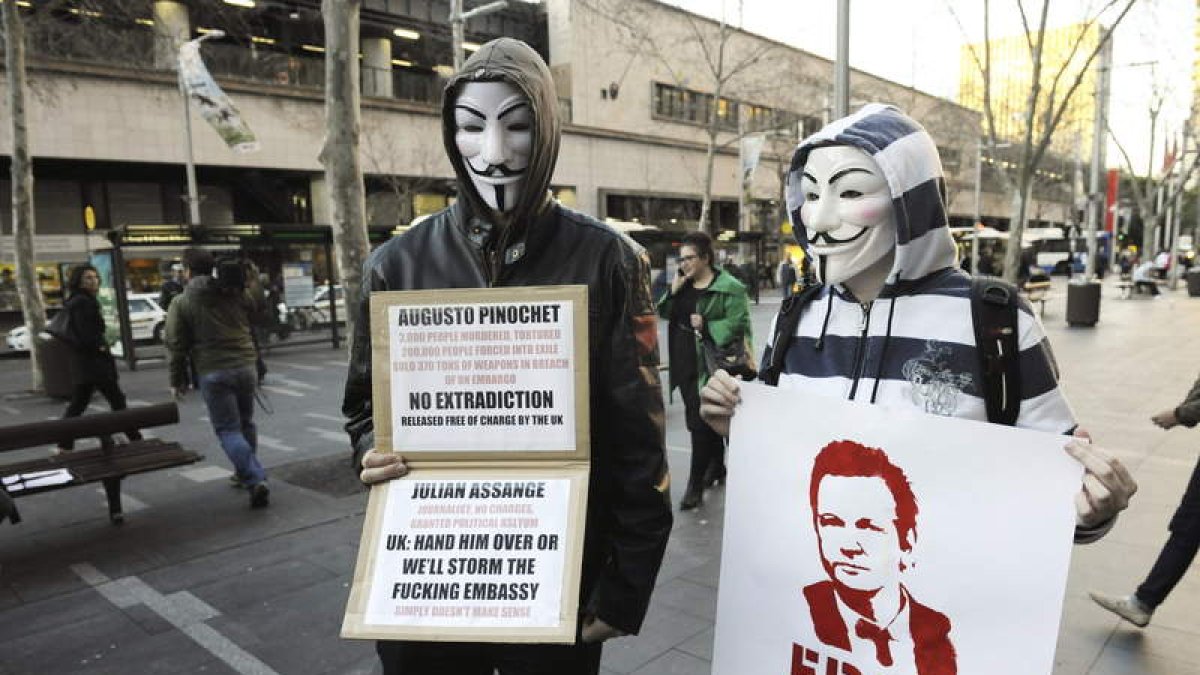 Dos manifestantes con máscaras de Anonymous sujetan pancartas de apoyo a Julian Assange.