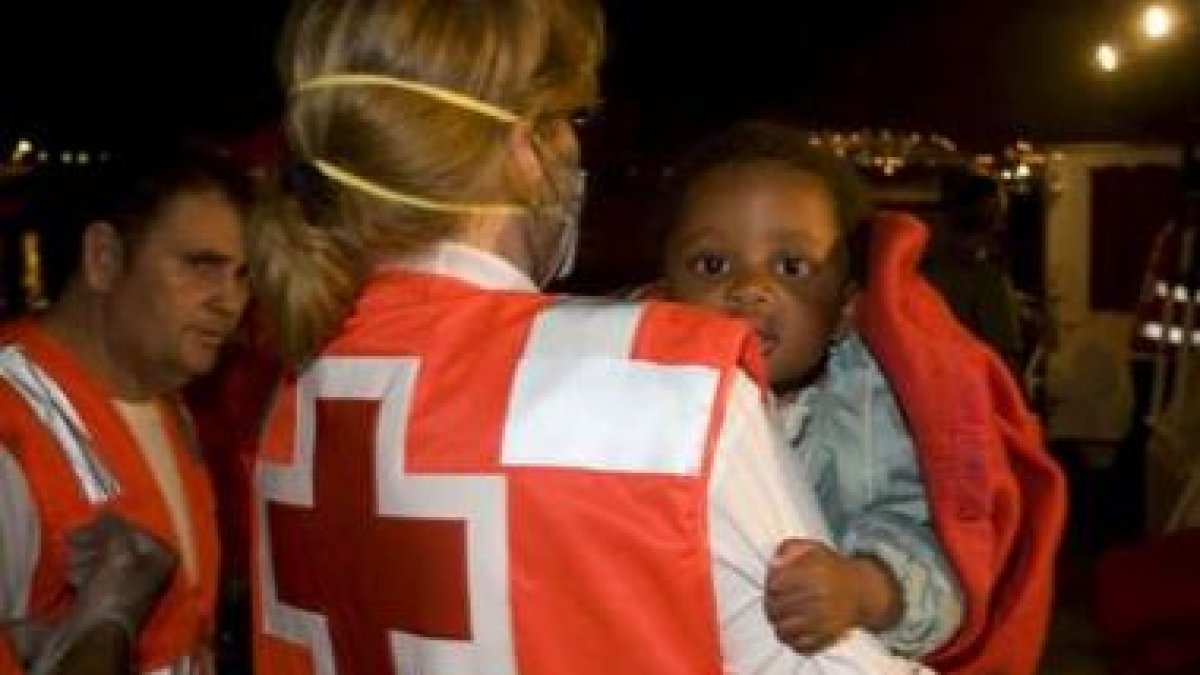 Un niño es recogido de una patera por un miembro de Cruz Roja Española