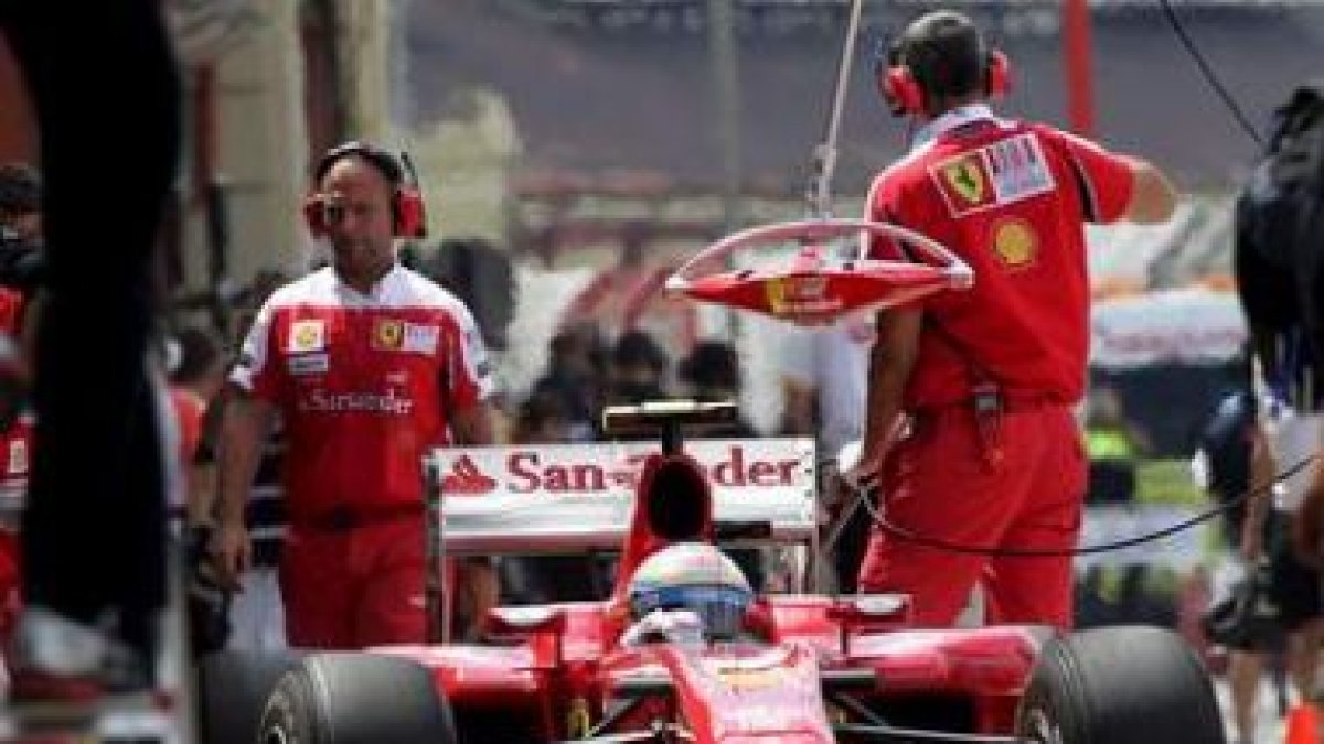 Alonso parado con su Ferrari en los boxes.