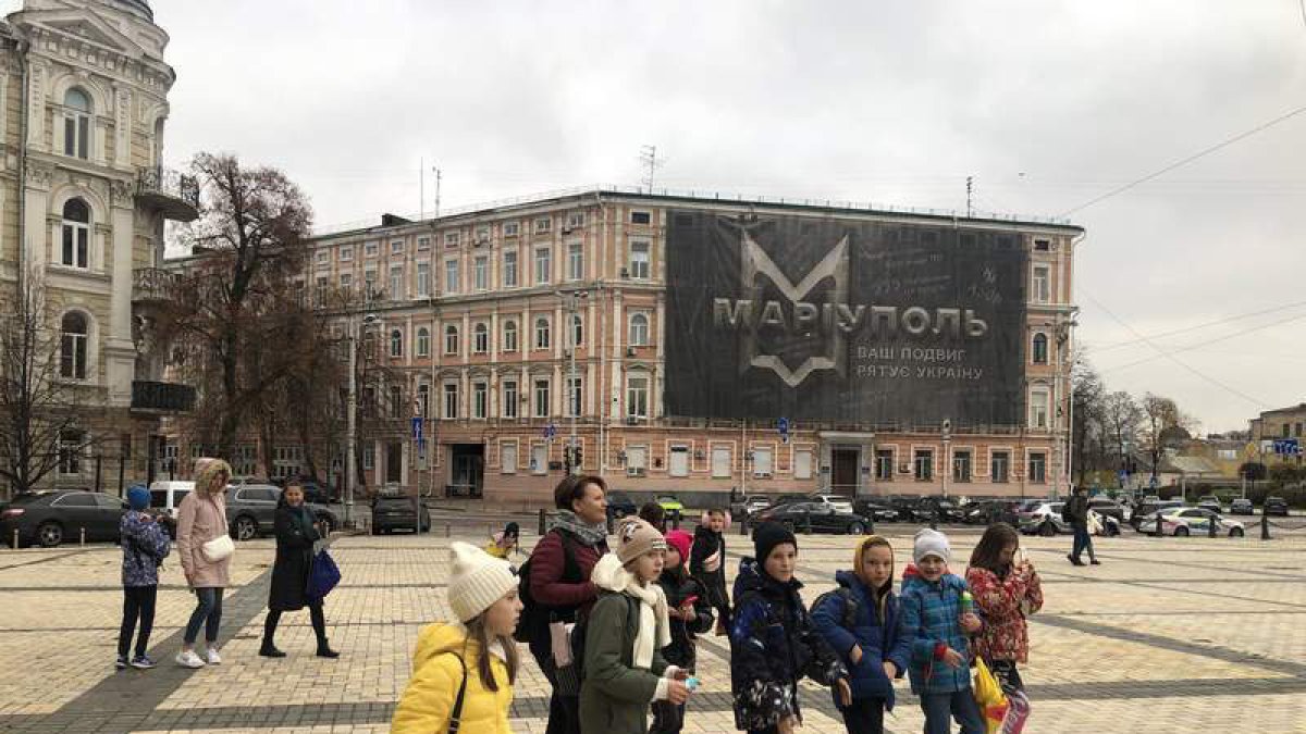 Un grupo de estudiantes se dirigen a la exposición ante un cartel recordando la hazaña de Mariupol. GERVASIO SÁNCHEZ