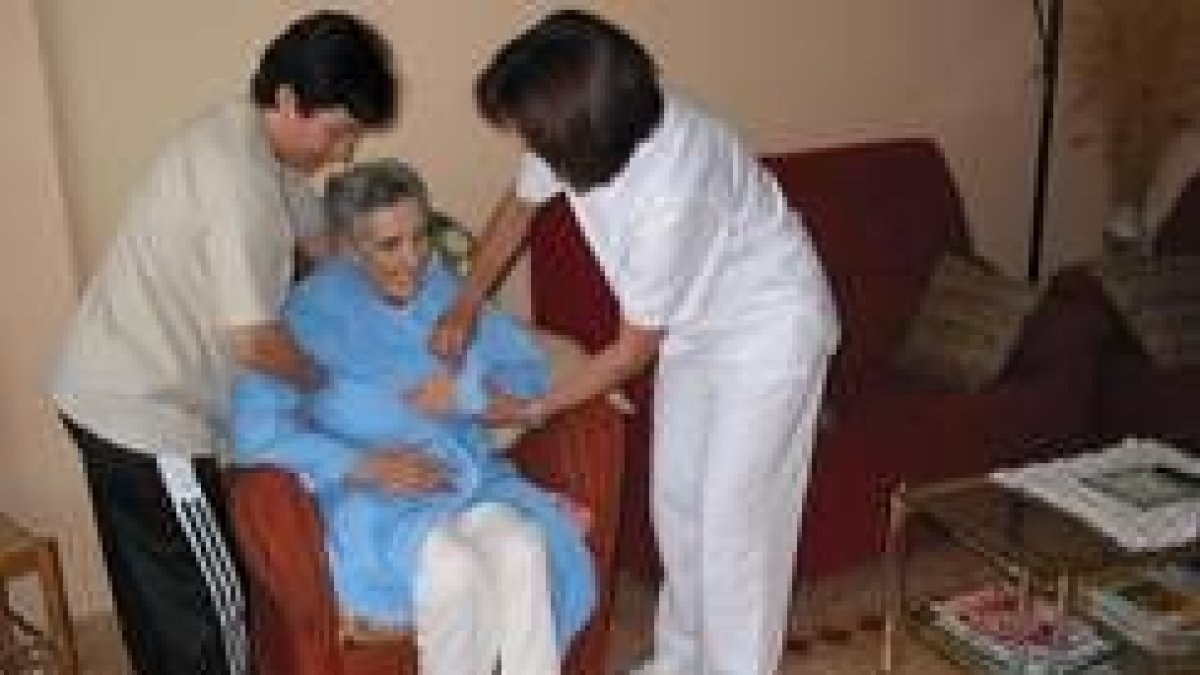 Una sanitaria y una familiar ayudan a incorporarse a una anciana aquejada de alzhéimer