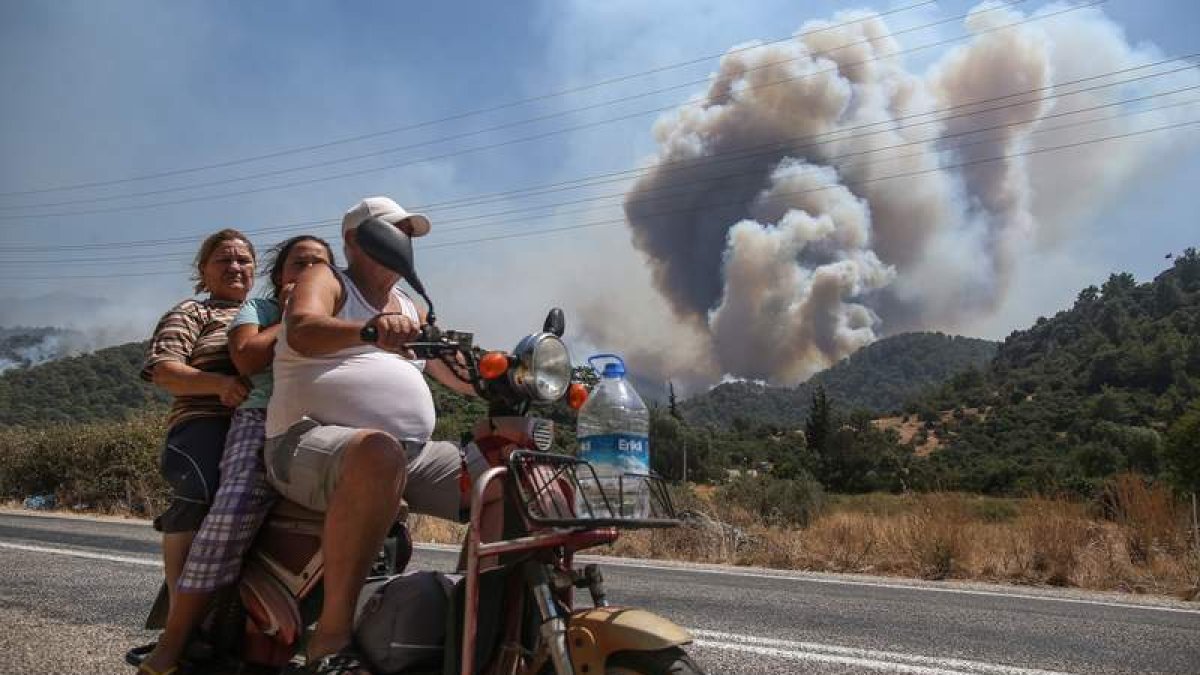 Una familia turca escapa con su motocicleta de la zona rural de Marmaris azotada por varios fuegos. ERDEM SAHIN