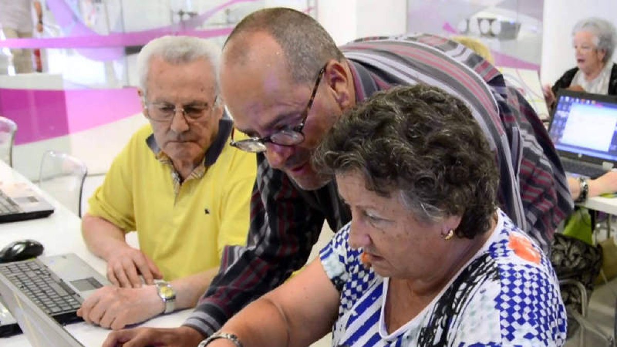 Laurentino López, en el centro, enseña a una mujer a manejar el ordenador en el centro CyL Digital de León. DL