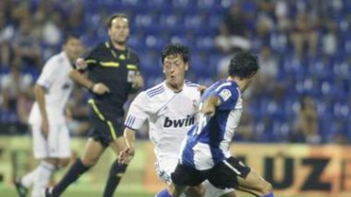 El debutante Mesut Özil (i), intenta marcharse del defensa del Hércules Francisco Peña (d).