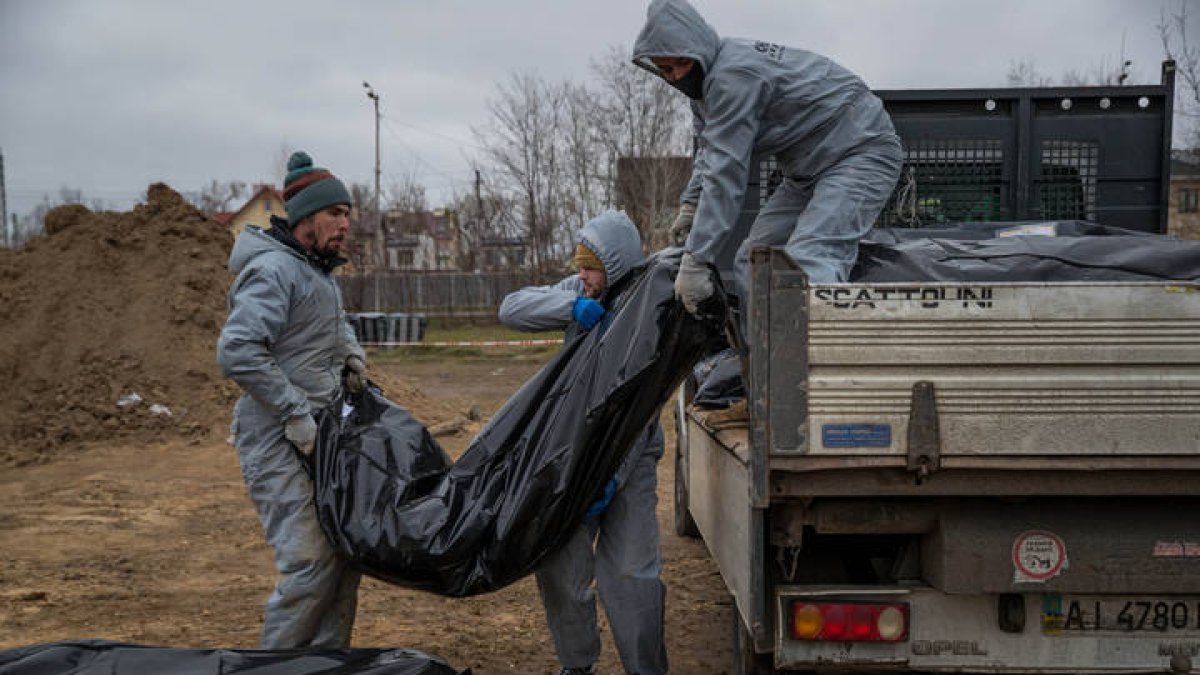 Autoridades forenses recogen cadáveres envueltos en plásticos para su traslado a la morgue, hoy, en Bucha (Ucrania). MIGUEL GUTIÉRREZ