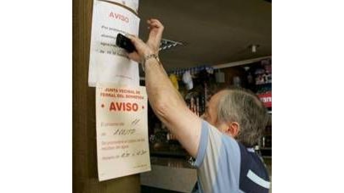Un vecino pega un cartel en que se indica las restricciones de agua