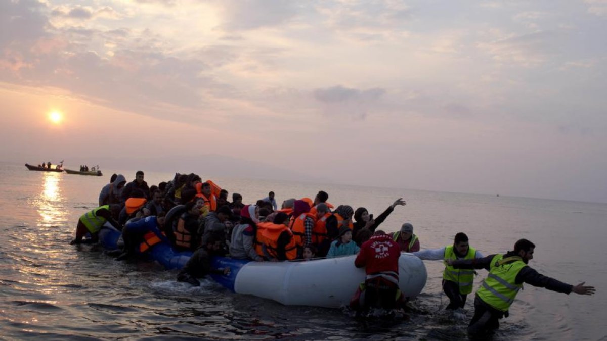 Varios voluntarios ayudan a un grupo de refugiaos a llegar a la costa, en la isla griega de Lesbos, el pasado marzo.