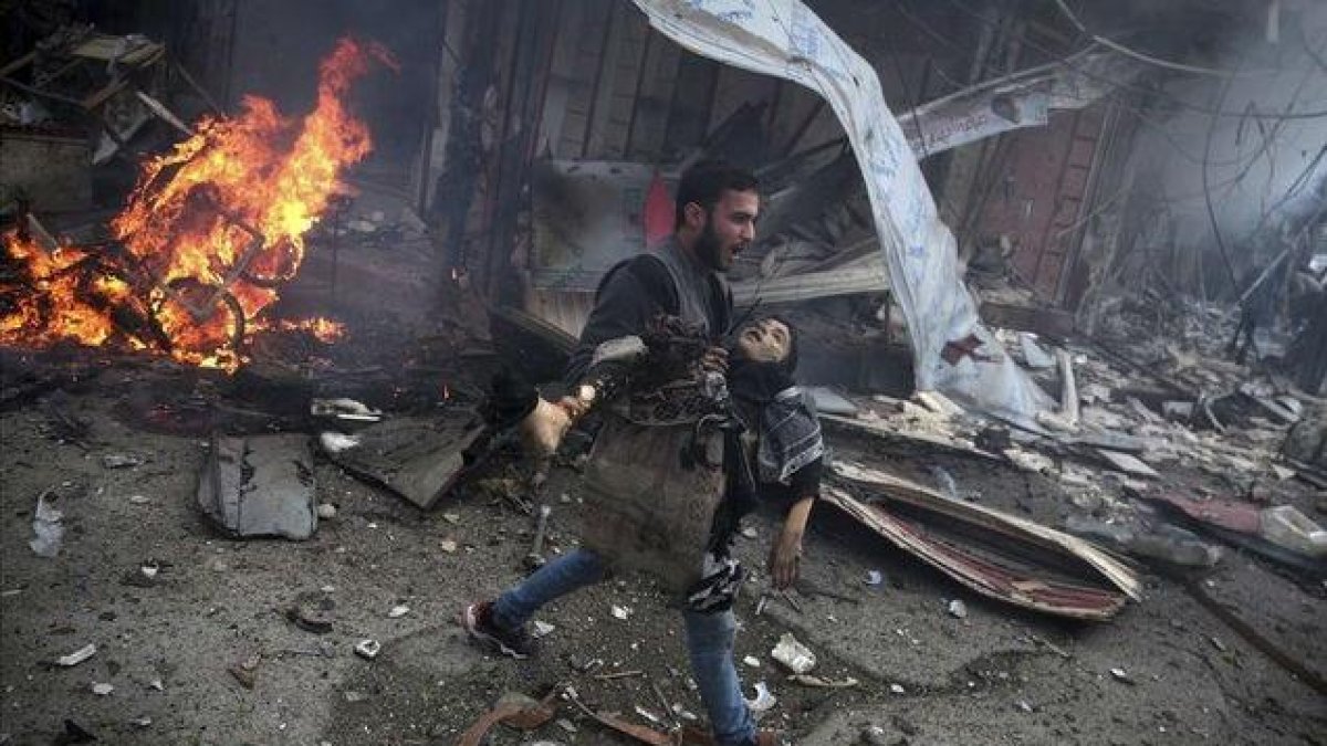 Un hombre sirio portando el cuerpo sin vida de un niño asesinado durante los bombardeos efectuados en la ciudad de Douma, Siria.