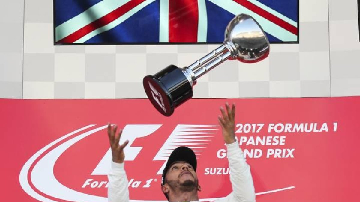 Lewis Hamilton lanza el trofeo de ganador del GP de Japón al aire ante la mirada de Max Verstappen, a la izquierda, y Daniel Ricciardo.