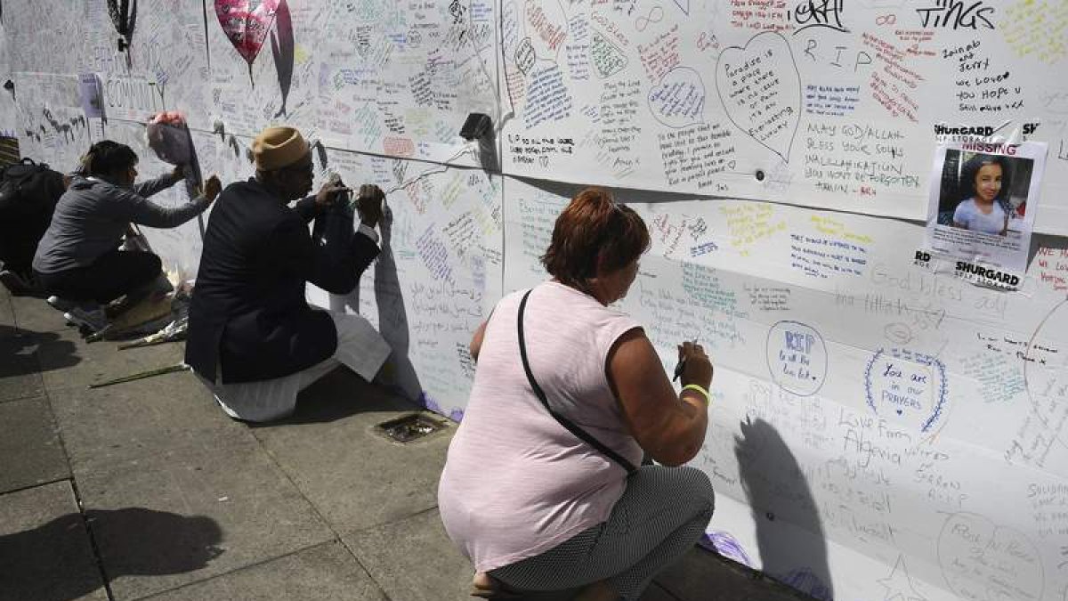 Varias personas escriben mensajes de condolencia junto a la Grenfell Tower. ANDY RAIN