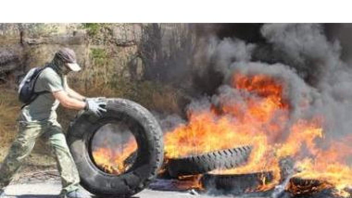 Un manifestante desplaza una rueda para abastecer de material inflamable la barricada situada a la e