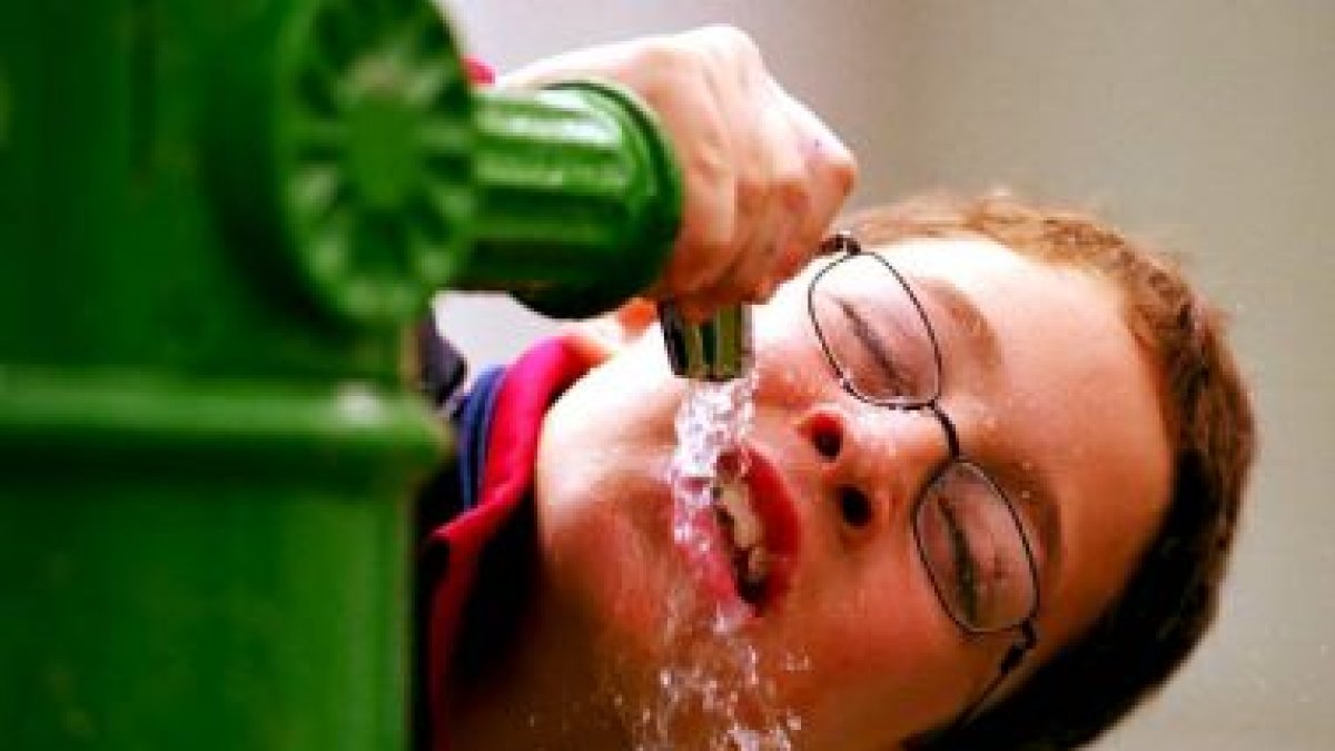 Imagen de un niño bebiendo agua en una fuente, debido al calor del verano
