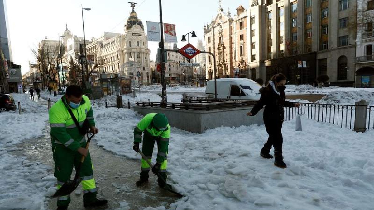 Dos operarios limpian las aceras de la calle Alcalá en Madrid mientras pasa una peatona. MARISCAL