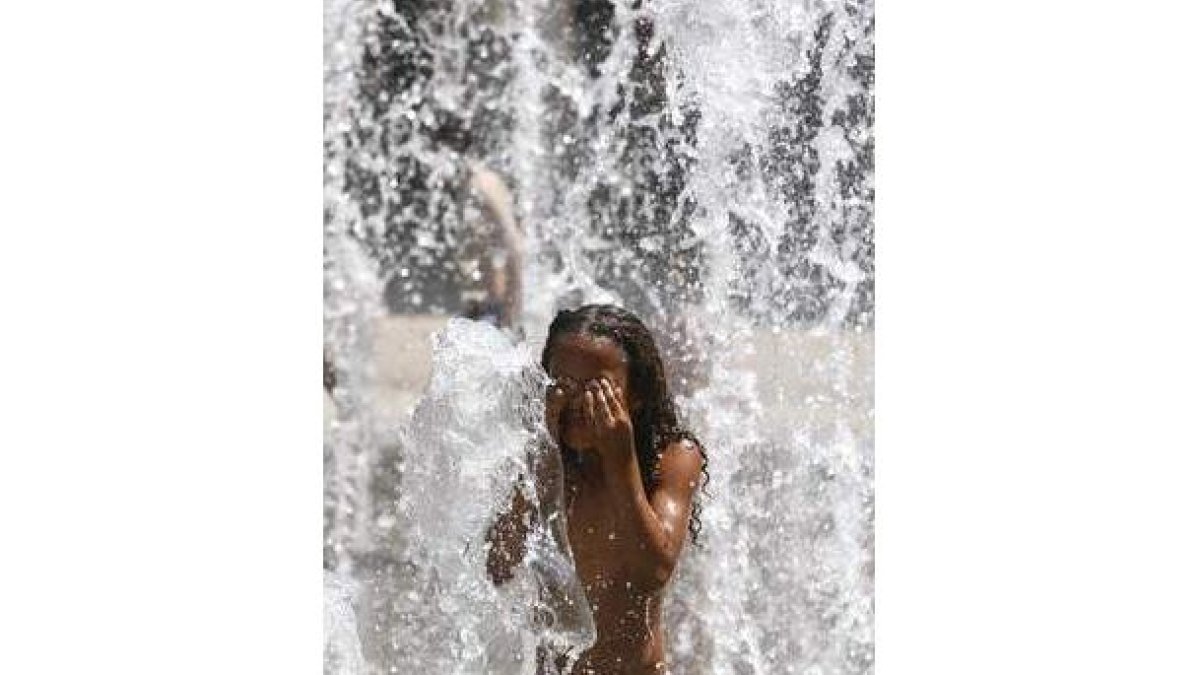 Una niña se refresca en una fuente de agua.