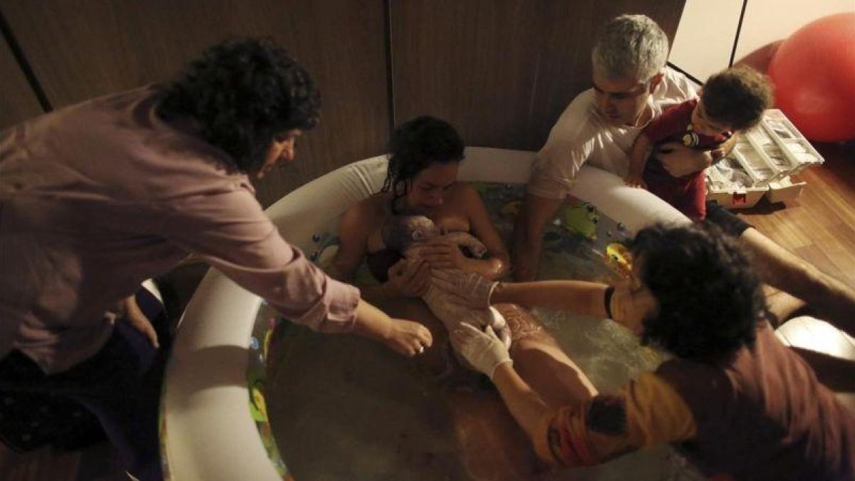 Una mujer da a luz en su casa, dentro de una piscina de agua caliente y rodeada de su familia y otros asistentes.