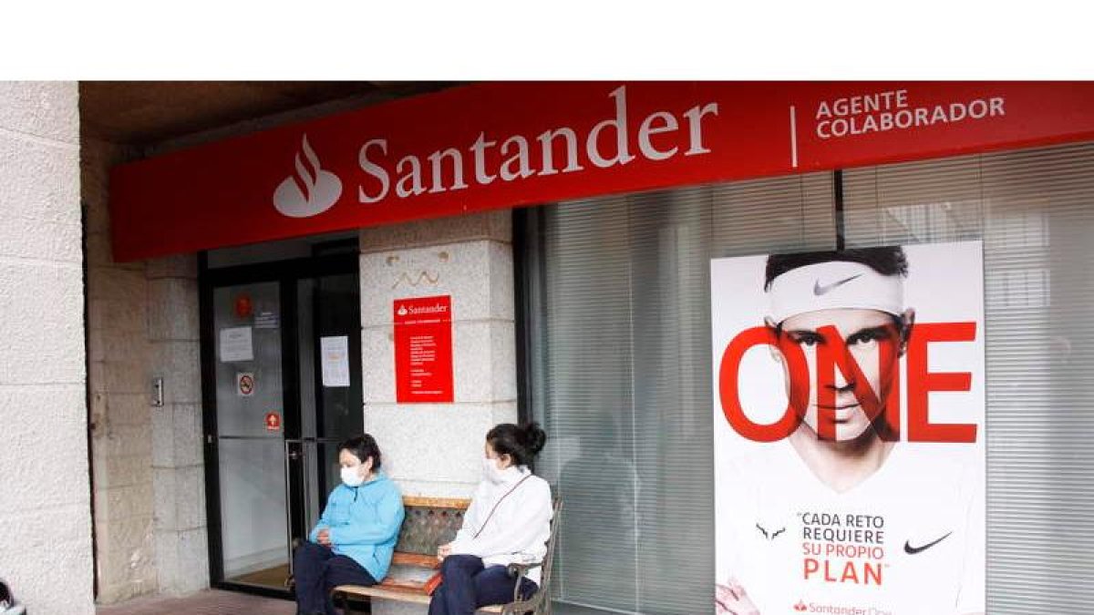 Dos mujeres charlan junto a la oficina de banco Santander que hace unos meses cerró en Riaño. CAMPOS