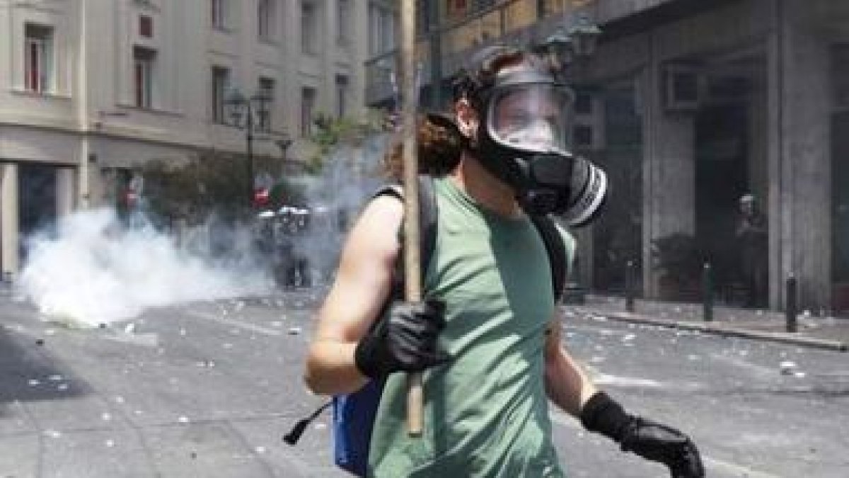 Un manifestante con una máscara de gas huye del lugar donde se concentran los antidisturbios.