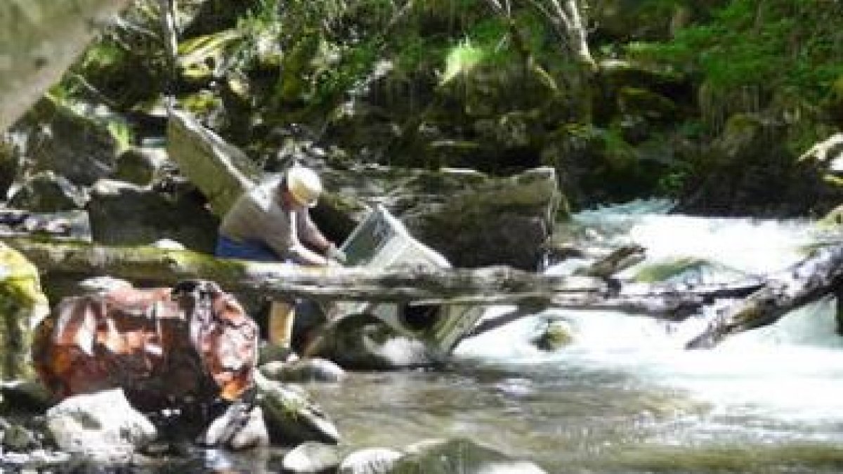 Un pescador se esfuerza para recuperar de las aguas del río una lavadora.