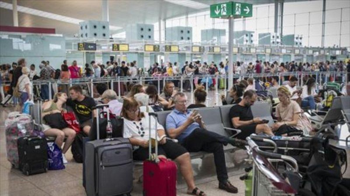 Colas frente al control de seguridad y pasajeros esperando en las instalaciones del aeropuerto de El Prat, ayer.