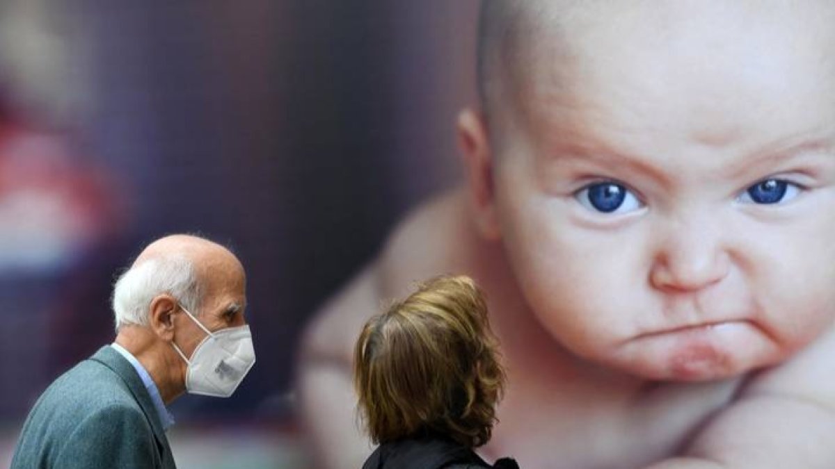 Dos personas con mascarilla pasan por delante de un cartel con la imagen de un bebé. DAL ZENNARO