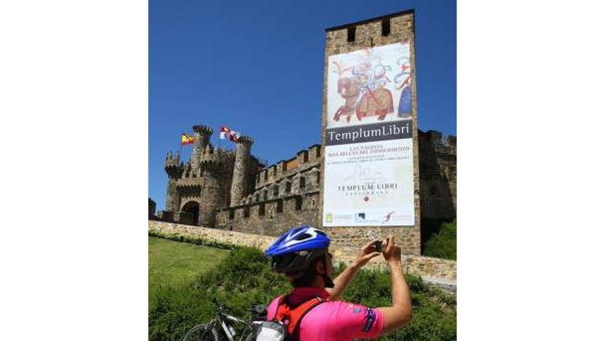 Un peregrino se detiene ante el castillo, con el cartel anunciando la exposición.