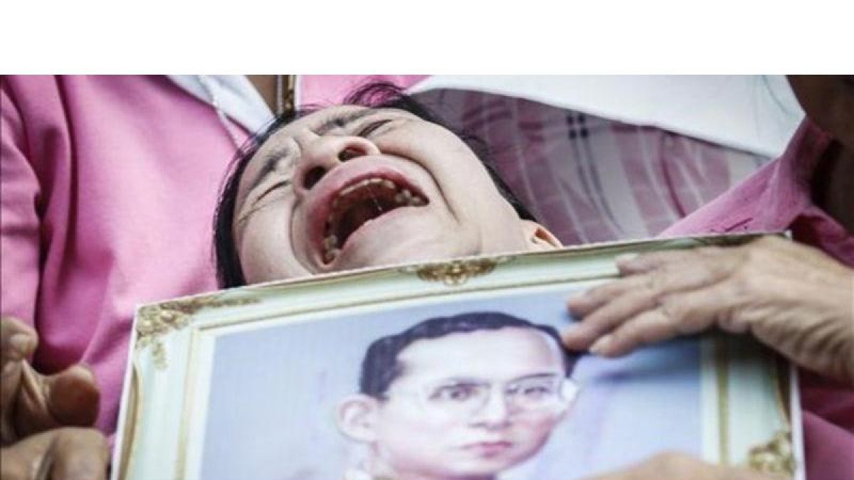 Una mujer llora a las puertas del hospital con la la foto del rey Bhumibol.