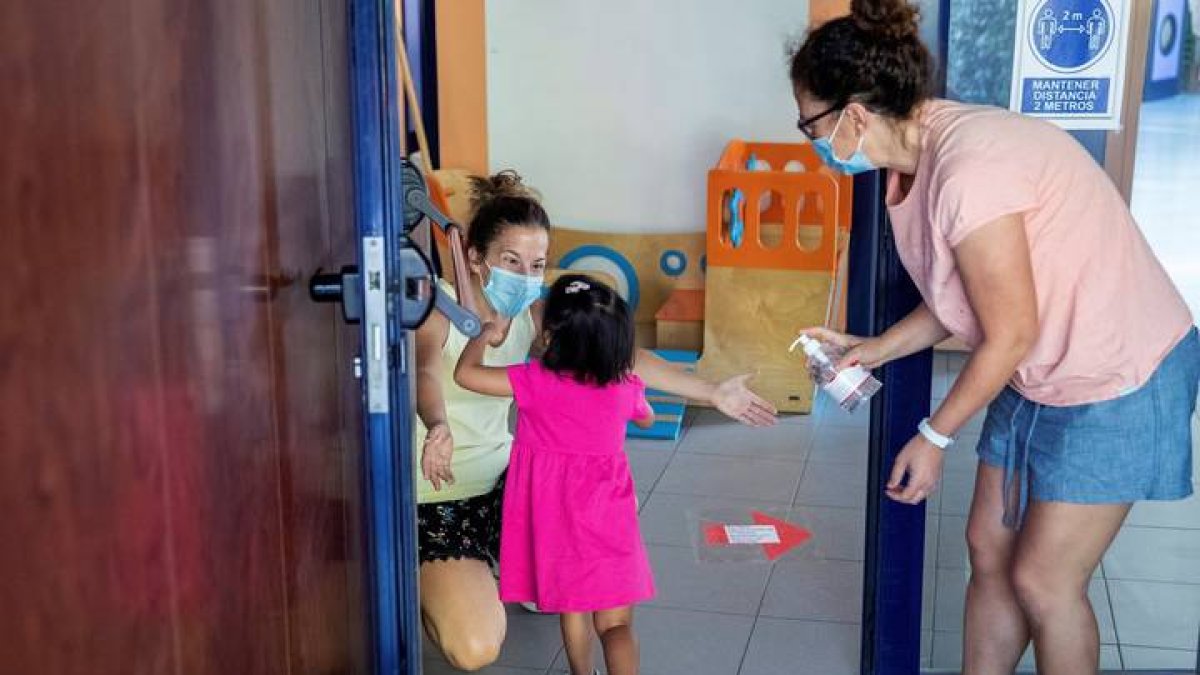Una educadora saluda a una niña durante la reapertura de la escuela infantil. RODRIGO JIMÉNEZ