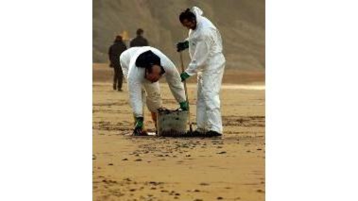 Dos operarios limpian el fuel de la playa vizcaína de Sopelana