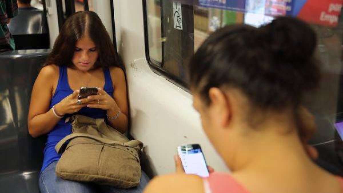 Dos chicas consultan en el metro sus respectivos móviles.