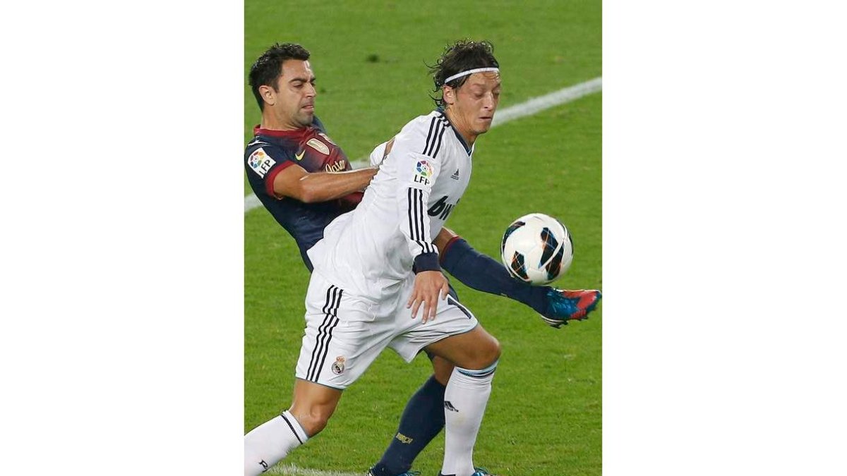 Xavi Hernández intenta robar la pelota al centrocampista alemán del Real Madrid Mesut Özil.