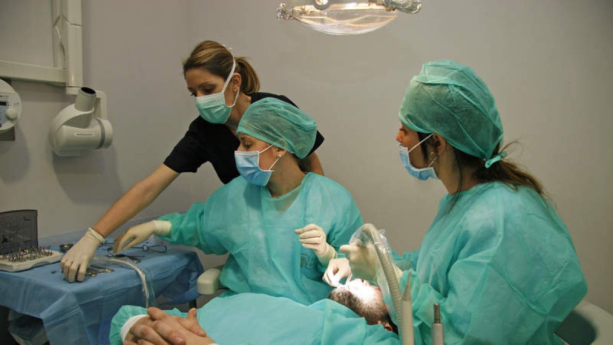 Uno de las pacientes de la Clínica Solidaria del Colegio de Dentistas de León se somete a un tratamiento ante la atenta mirada de dos alumnos. F. OTERO PERANDONES