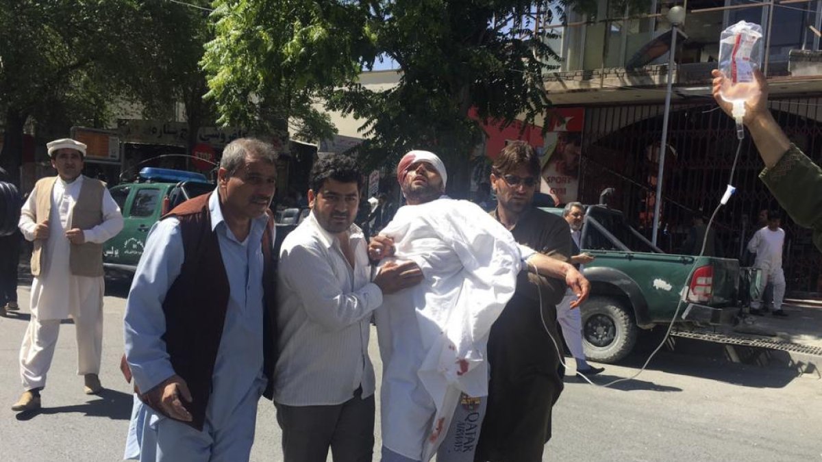 Tres personas ayudan a un hombre herido en el atentado de este miércoles en Kabul.