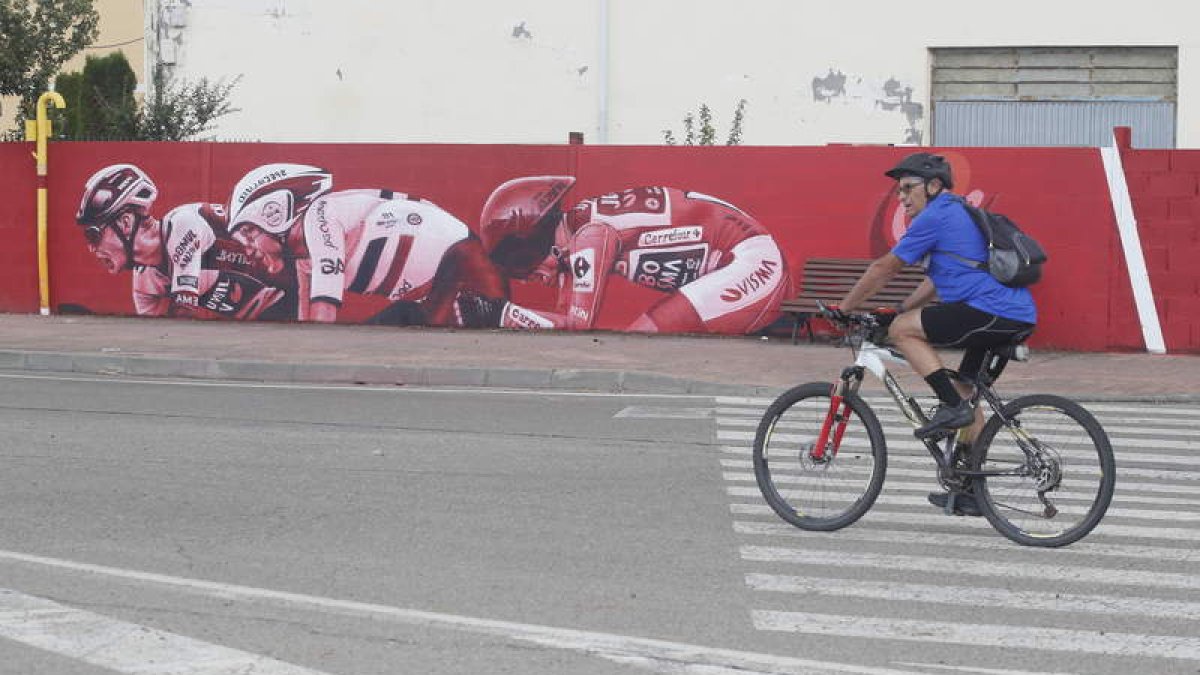 Un ciclista pasa por delante del mural alusivo a la Vuelta a España 2023 situado en la calle Julio Hernández de La Bañeza. RAMIRO