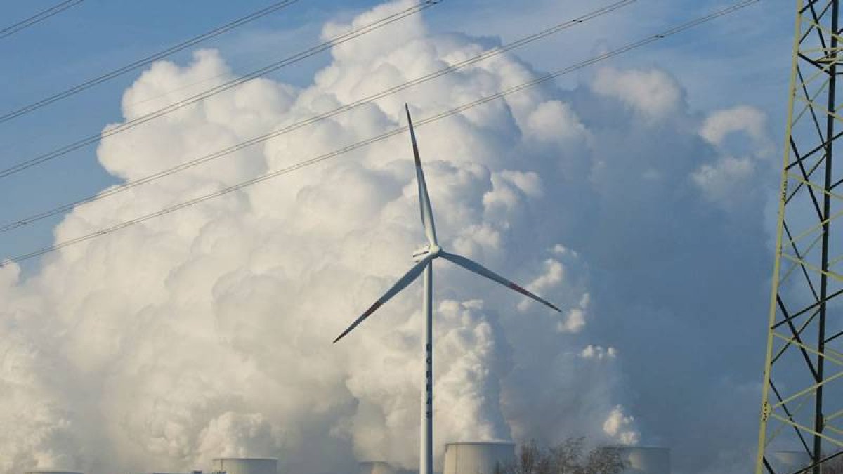 Una turbina de energía eólica enfrente de las torres de una planta de energía.