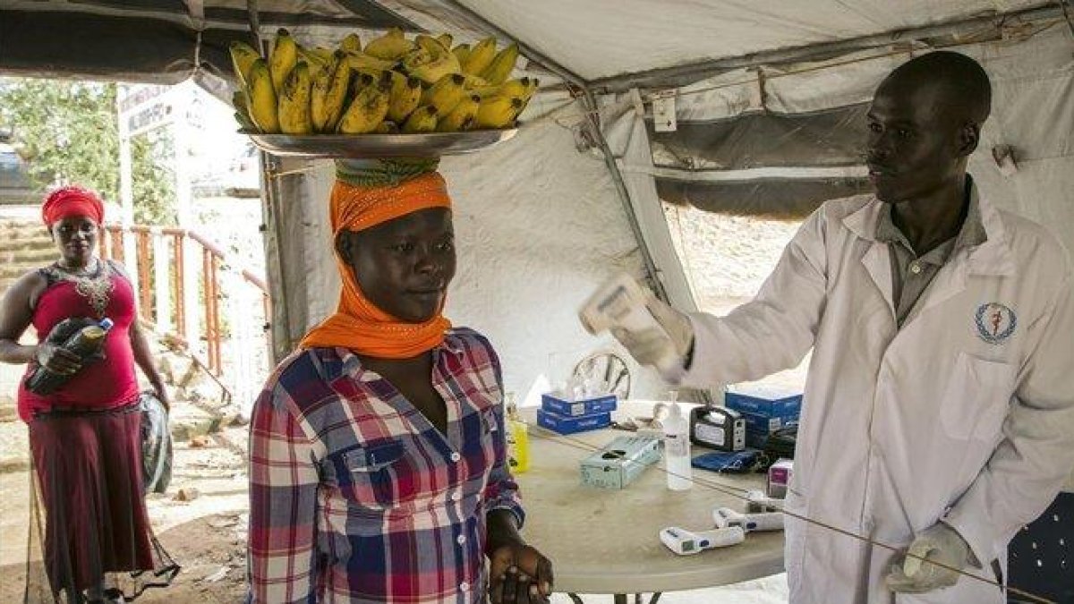 Un trabajador sanitario comprueba el estado de varias personas en la frontera de Nimule, en Uganda.