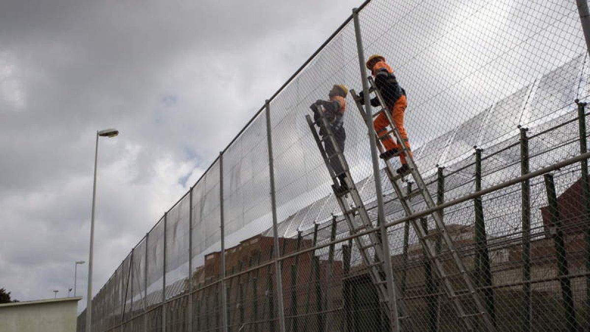 Dos operarios trabajan en la instalación de malla antitrepa entre Melilla y Marruecos.