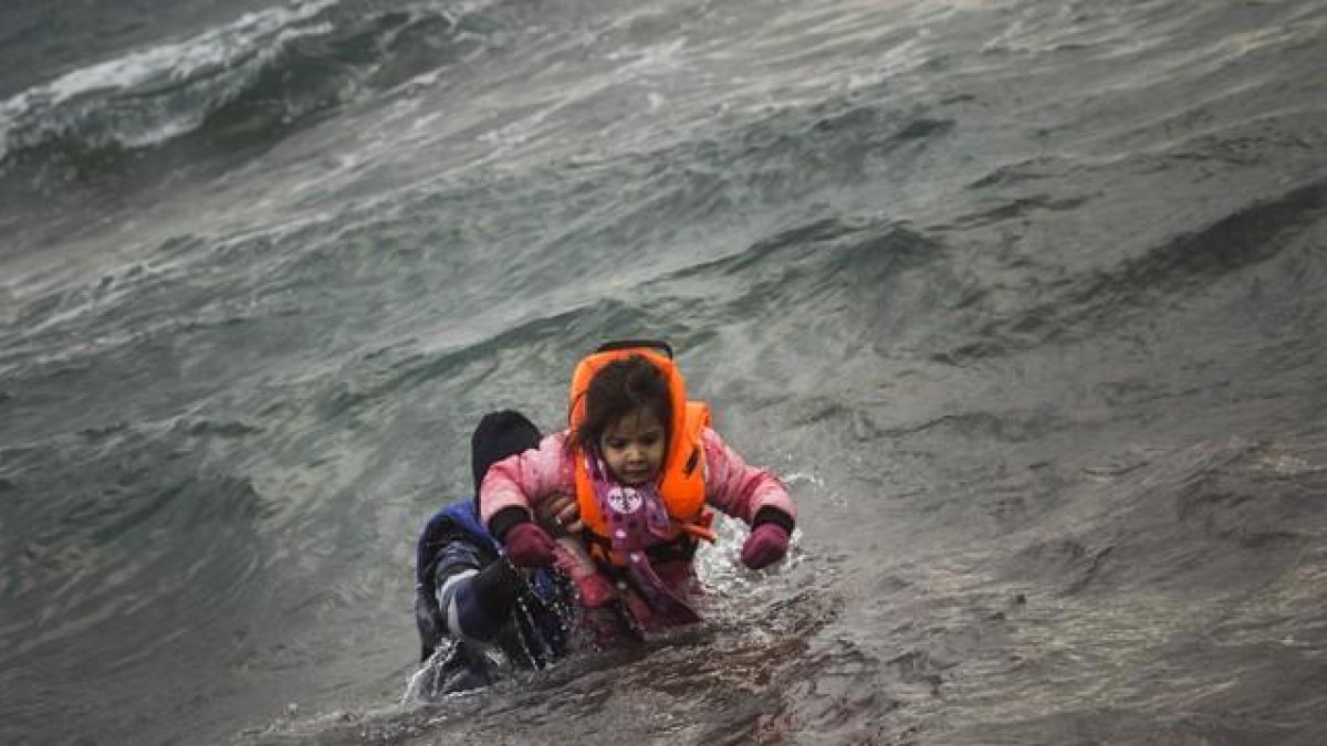 Un hombre ayuda a un niño cuyo barco ha naufragado este domingo en el Egeo.