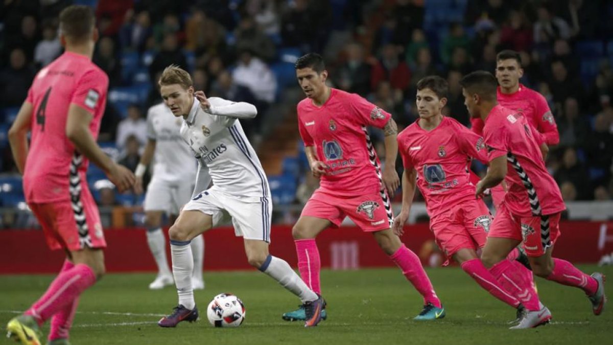 El centrocampista noruego del Real Madrid Martin Odegaard, defiende el balón entre varios jugadores de la Cultural.