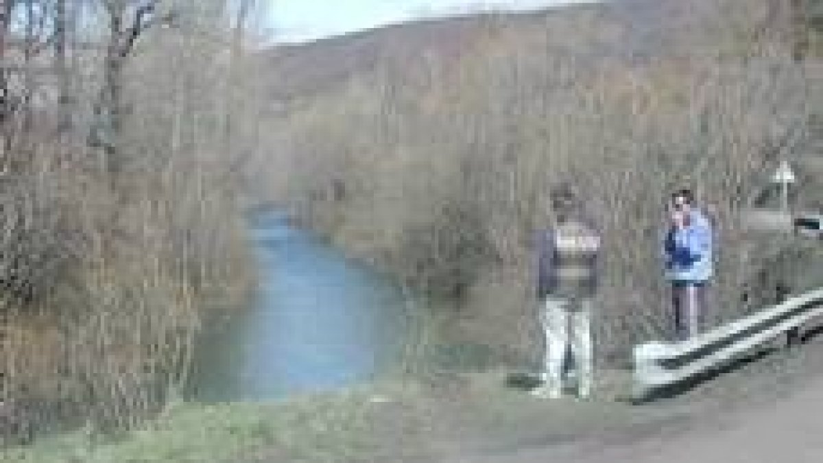Dos personas observan el lugar concreto de la carretera por el que el vehículo se precipitó al río